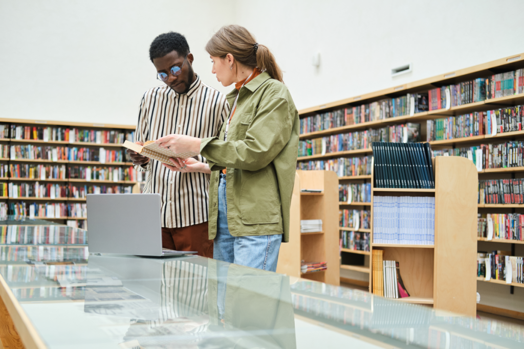 Foto seorang laki-laki kulit hitam dan seorang perempuan kulit putih yang sedang membaca buku di sebuah perpustakaan